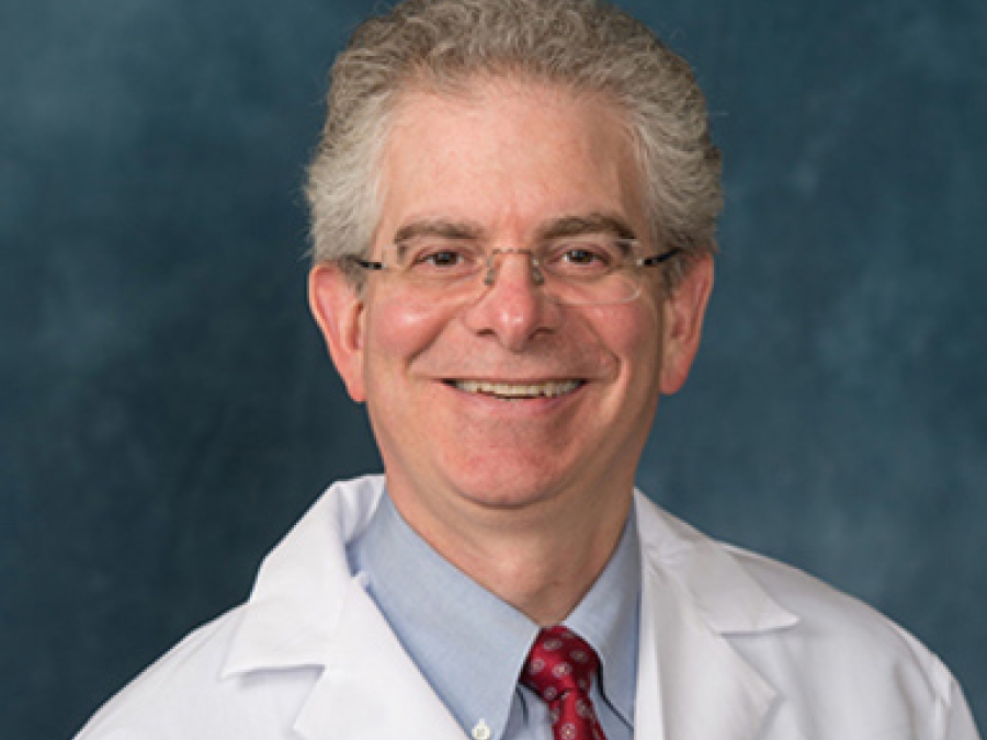 Smiling portrait of John Ayanian, M.D., MPP.  He has short gray hair and is wearing glasses, a red tie, and a white lab coat.