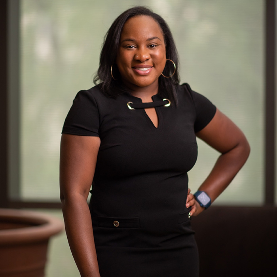 Black woman wearing black dress with one hand on hip and smiling