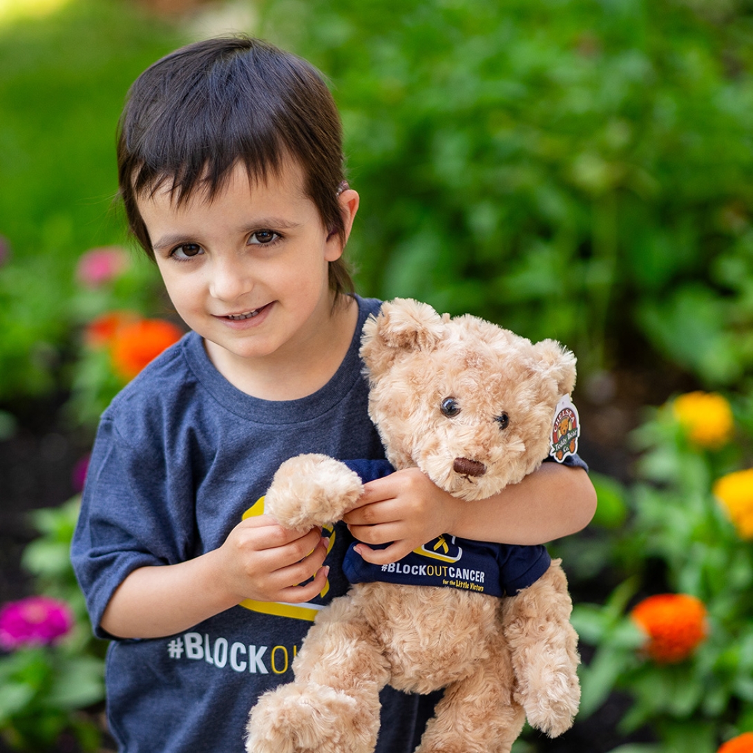 Boy holding a golden brown teddy bear. Both wearing the block out cancer t-shirt.