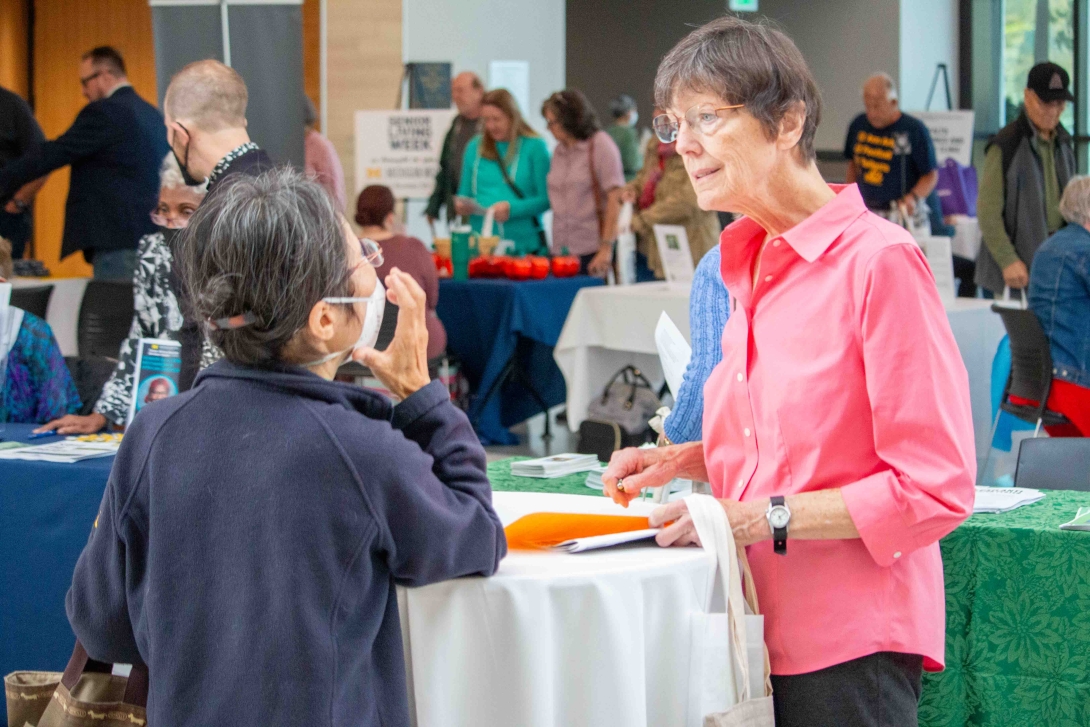 Two senior women speak at an expo booth